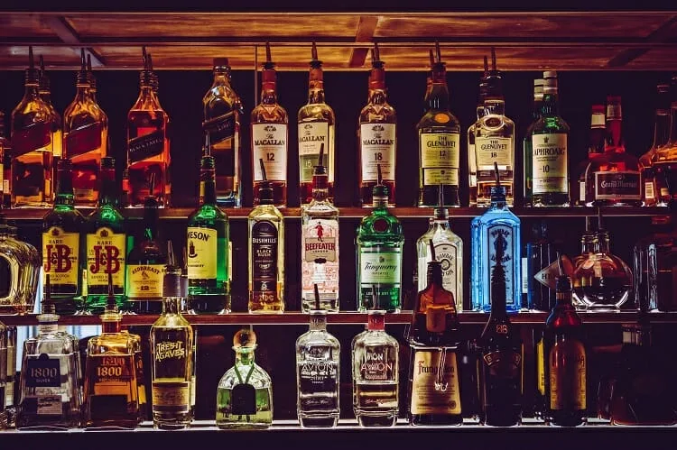 Prateleira cheia com várias garrafas de bebida alcoólica, de marcas variadas.