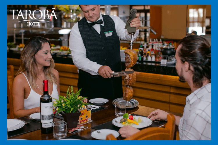 Casal sentado na mesa do Restaurante Bufalo, sendo servido pelo garçom no rodízio de carne. Restaurantes no centro de Foz do Iguaçu.